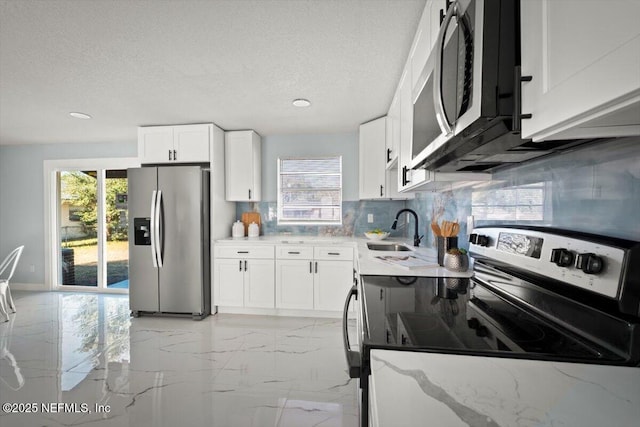 kitchen with a textured ceiling, appliances with stainless steel finishes, white cabinetry, sink, and light stone counters