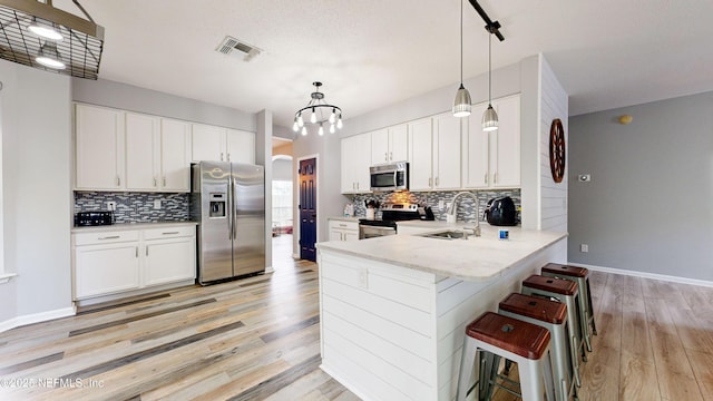 kitchen with pendant lighting, a breakfast bar, white cabinets, kitchen peninsula, and stainless steel appliances