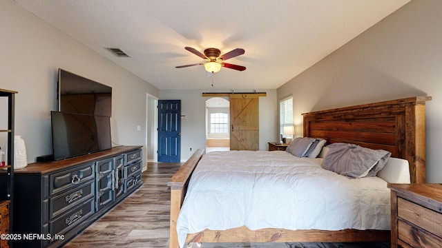 bedroom with a barn door, ceiling fan, a textured ceiling, and light wood-type flooring