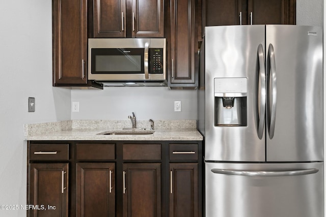 kitchen featuring dark brown cabinetry, light stone countertops, sink, and stainless steel appliances