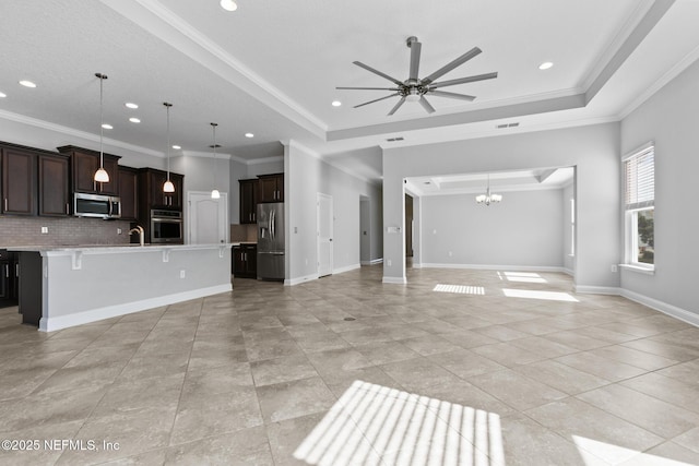 unfurnished living room featuring ceiling fan with notable chandelier, sink, ornamental molding, light tile patterned floors, and a tray ceiling