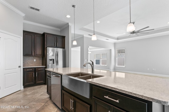 kitchen with sink, a raised ceiling, a textured ceiling, a kitchen island with sink, and appliances with stainless steel finishes