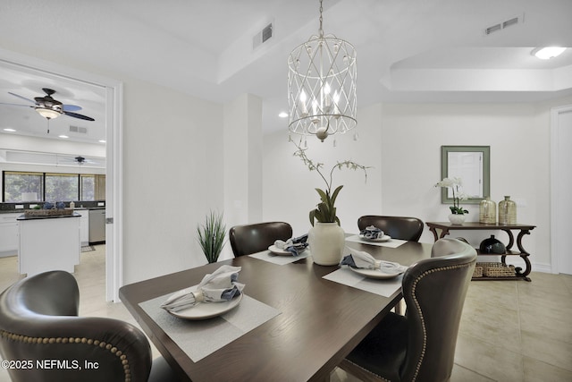 dining area with ceiling fan with notable chandelier and a tray ceiling