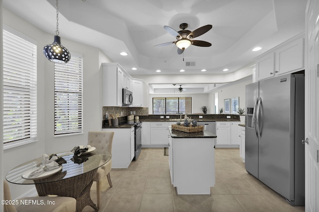 kitchen featuring white cabinetry, a center island, backsplash, a tray ceiling, and appliances with stainless steel finishes