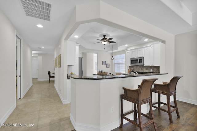 kitchen featuring kitchen peninsula, stainless steel appliances, a raised ceiling, white cabinets, and ceiling fan