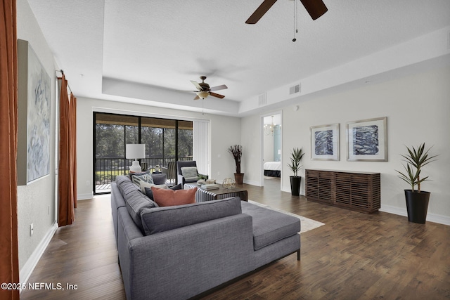 living room featuring ceiling fan, dark wood-type flooring, a raised ceiling, and a textured ceiling