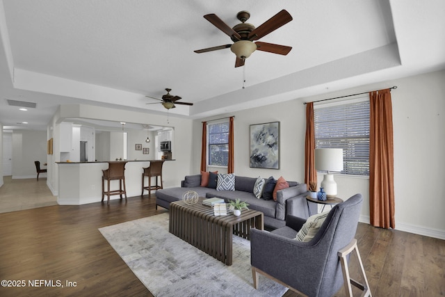 living room featuring ceiling fan, a tray ceiling, and dark hardwood / wood-style floors