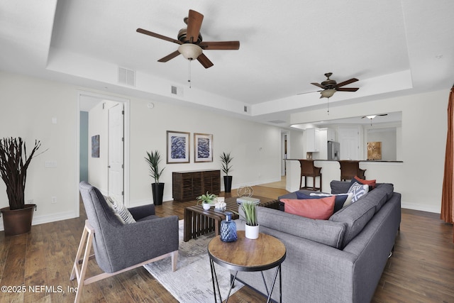 living room featuring ceiling fan, dark hardwood / wood-style flooring, and a tray ceiling