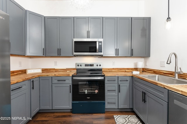 kitchen with sink, hanging light fixtures, stainless steel appliances, butcher block countertops, and gray cabinets