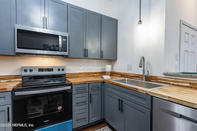 kitchen featuring appliances with stainless steel finishes, butcher block countertops, pendant lighting, and sink