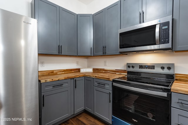 kitchen featuring gray cabinetry, dark hardwood / wood-style floors, stainless steel appliances, and wooden counters