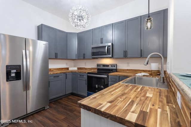 kitchen with sink, hanging light fixtures, wooden counters, a notable chandelier, and appliances with stainless steel finishes