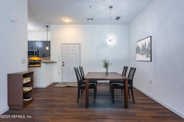 dining area with sink, dark wood-type flooring, and an inviting chandelier