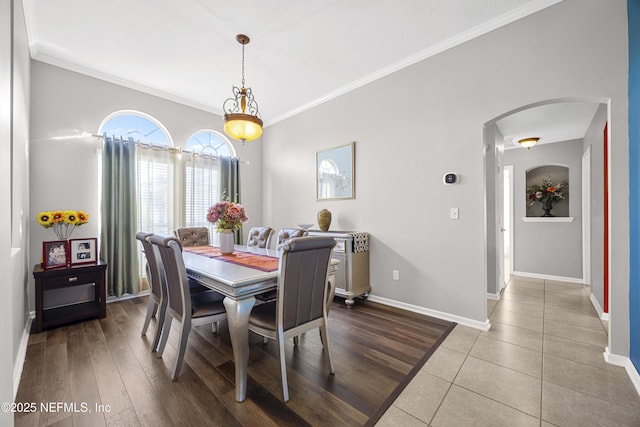 dining space featuring arched walkways, baseboards, wood finished floors, and crown molding