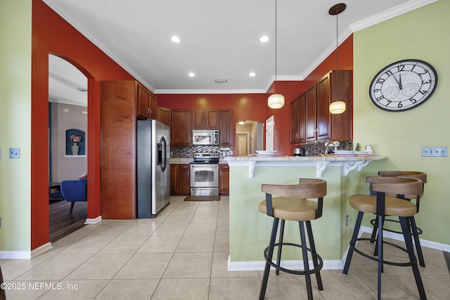 kitchen with arched walkways, a peninsula, light countertops, appliances with stainless steel finishes, and pendant lighting