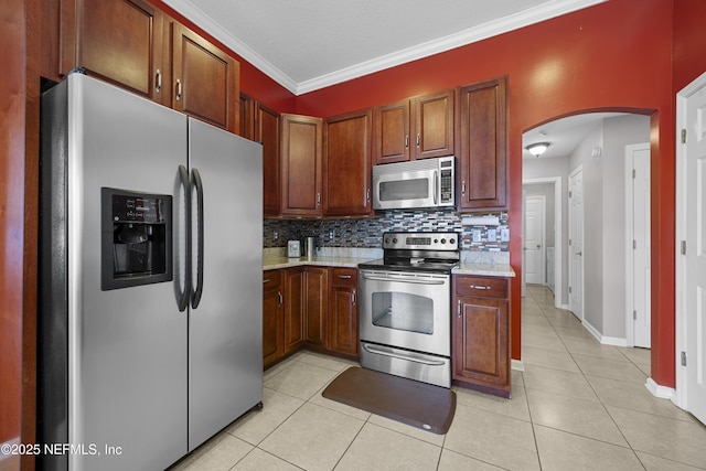 kitchen featuring arched walkways, light tile patterned floors, stainless steel appliances, ornamental molding, and decorative backsplash