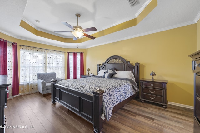 bedroom featuring visible vents, baseboards, dark wood-style floors, a tray ceiling, and crown molding