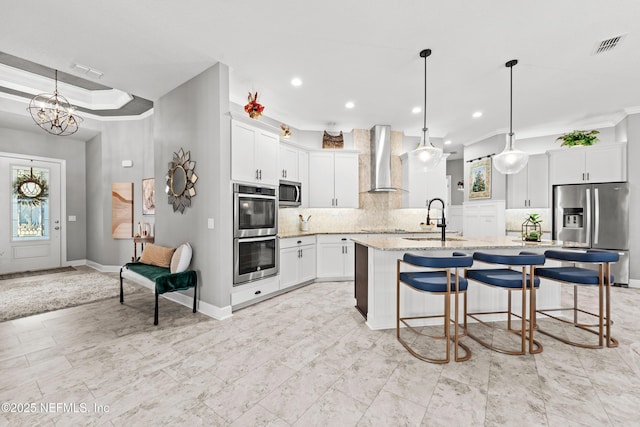 kitchen with stainless steel appliances, sink, wall chimney range hood, pendant lighting, and white cabinets