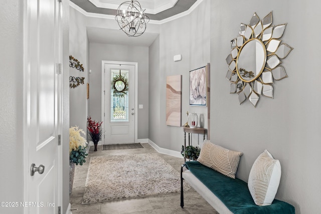 entryway with a raised ceiling, ornamental molding, and an inviting chandelier