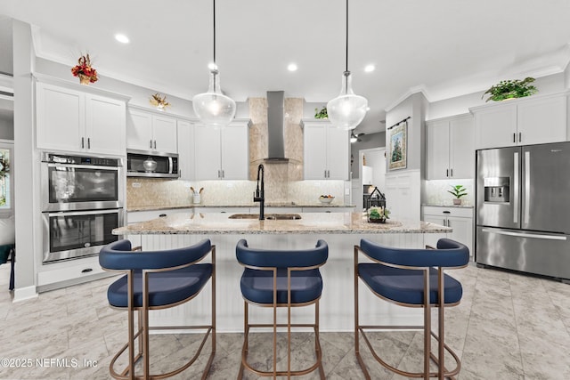 kitchen with light stone countertops, stainless steel appliances, a kitchen island with sink, sink, and wall chimney range hood