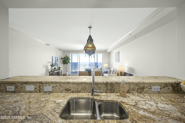 kitchen with ornamental molding, light stone countertops, sink, and hanging light fixtures