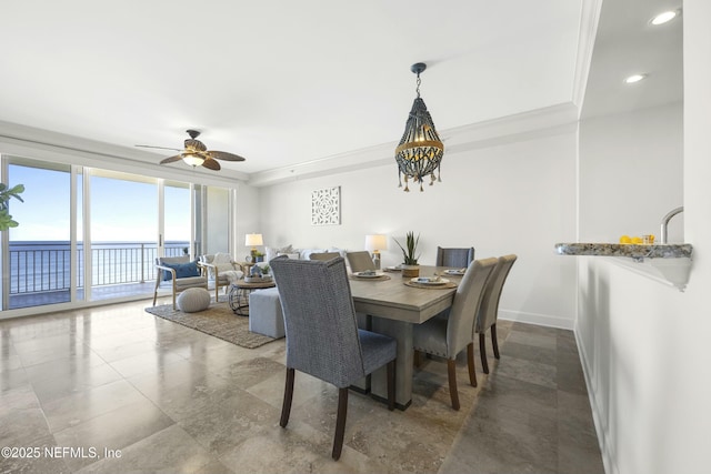 dining area with floor to ceiling windows, ceiling fan, a tray ceiling, a water view, and ornamental molding