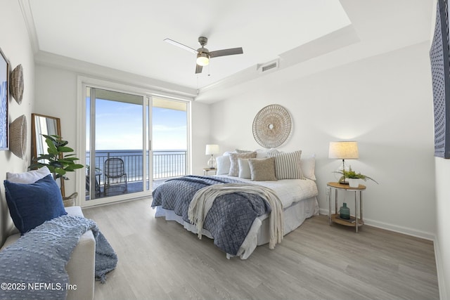 bedroom with access to exterior, a tray ceiling, ceiling fan, a water view, and hardwood / wood-style flooring