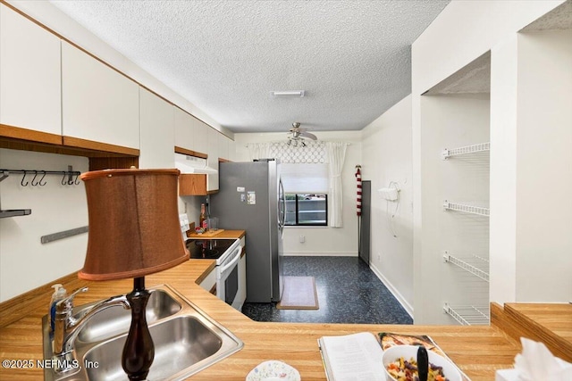 kitchen with stainless steel fridge, a textured ceiling, ceiling fan, sink, and white electric stove