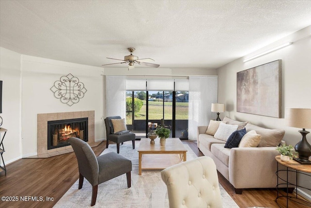 living room with hardwood / wood-style floors, ceiling fan, a textured ceiling, and a tiled fireplace