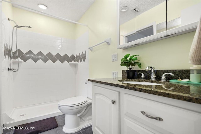 bathroom featuring vanity, toilet, tiled shower, and a textured ceiling