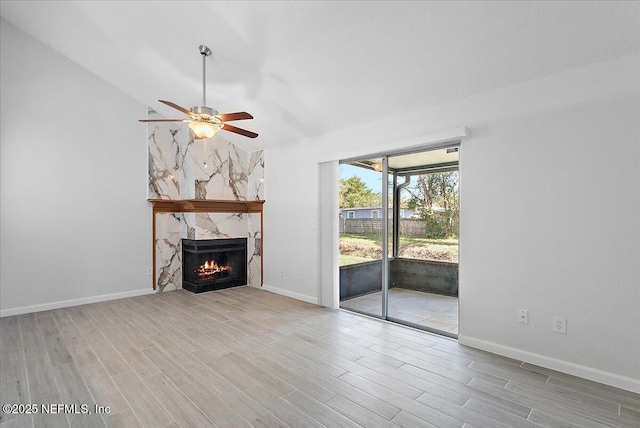 unfurnished living room featuring ceiling fan, light wood-type flooring, a premium fireplace, and vaulted ceiling