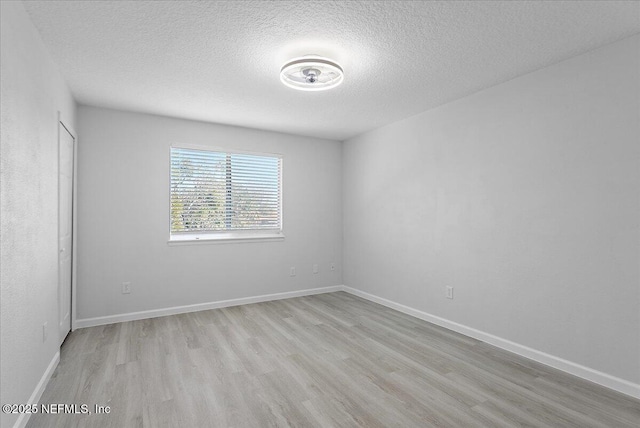 empty room with a textured ceiling, light wood finished floors, and baseboards