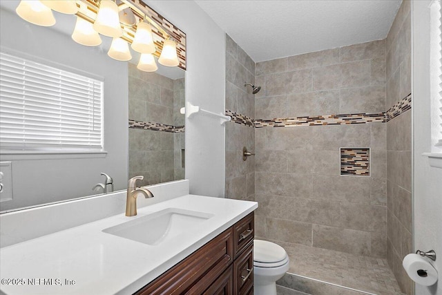 bathroom with toilet, a tile shower, and vanity