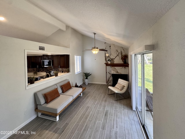 living area featuring wood finish floors, vaulted ceiling with beams, visible vents, a stone fireplace, and a textured ceiling