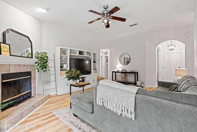 living room with a textured ceiling, ceiling fan with notable chandelier, wood-type flooring, and a fireplace