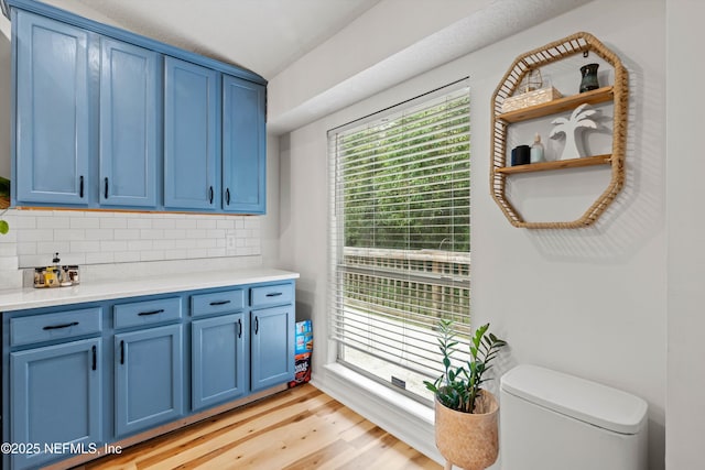 interior space with backsplash, light hardwood / wood-style flooring, blue cabinets, and vaulted ceiling