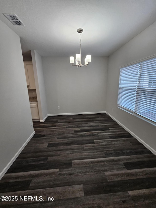 unfurnished dining area with dark wood-type flooring and an inviting chandelier