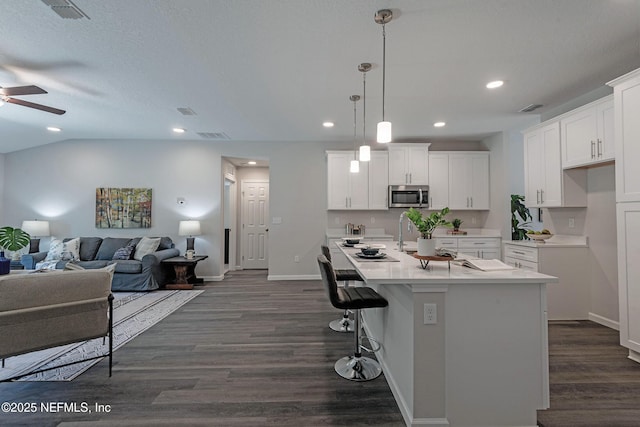 kitchen featuring dark hardwood / wood-style flooring, a kitchen island with sink, ceiling fan, decorative light fixtures, and white cabinets