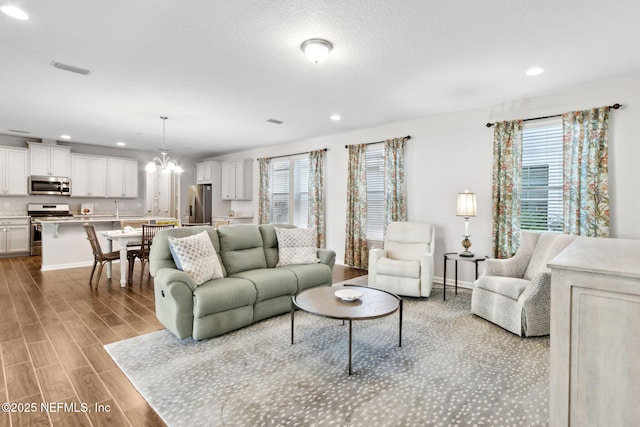 living area featuring visible vents, an inviting chandelier, wood finished floors, and a healthy amount of sunlight