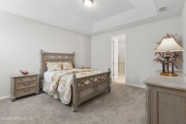 bedroom featuring baseboards, a raised ceiling, ensuite bath, visible vents, and light carpet