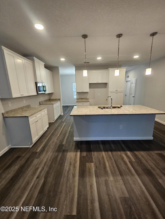 kitchen with sink, dark hardwood / wood-style floors, white cabinetry, hanging light fixtures, and an island with sink