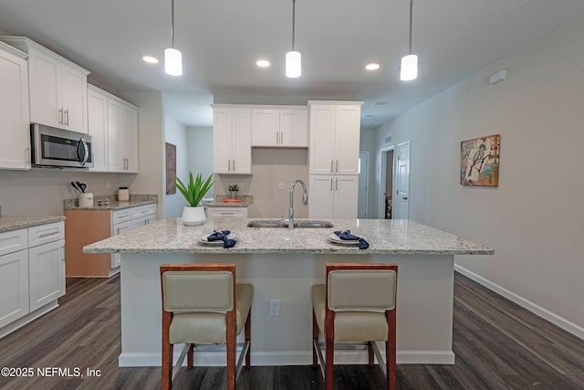 kitchen featuring white cabinets, pendant lighting, a kitchen island with sink, and sink