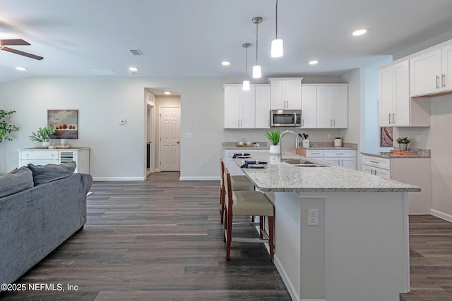 kitchen with a center island with sink, white cabinetry, sink, and hanging light fixtures