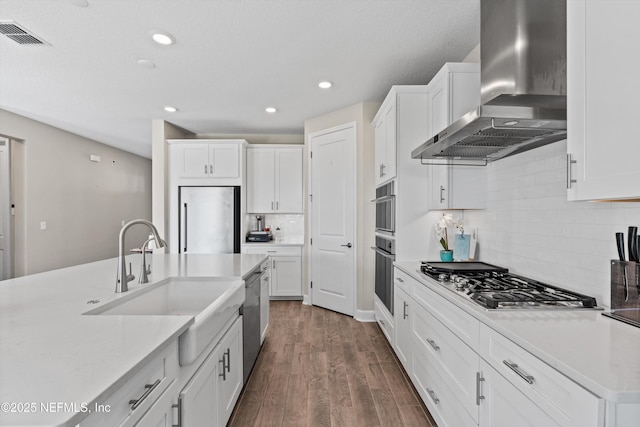 kitchen with white cabinetry, sink, stainless steel appliances, dark wood-type flooring, and wall chimney range hood