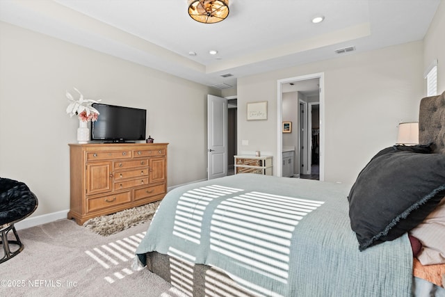 carpeted bedroom featuring ensuite bath and a tray ceiling