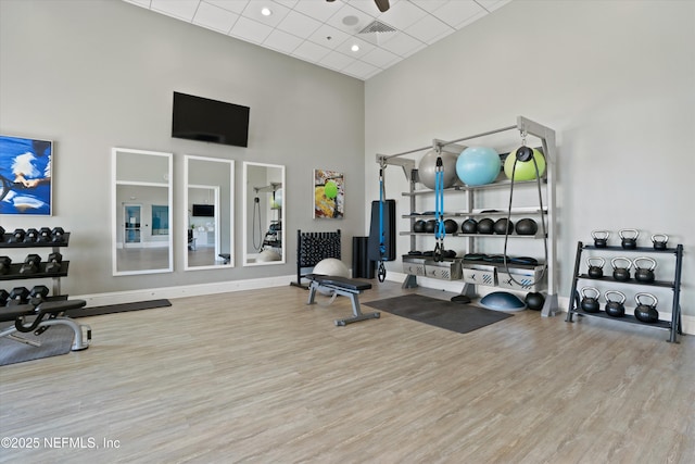 gym with hardwood / wood-style flooring, a towering ceiling, ceiling fan, and a paneled ceiling