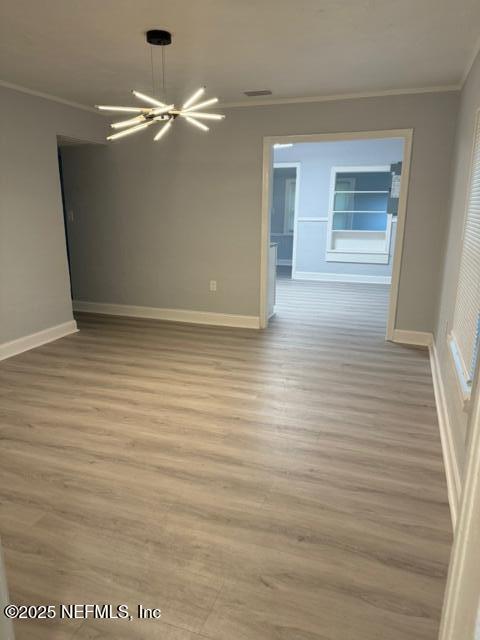 spare room with light hardwood / wood-style floors, ornamental molding, and an inviting chandelier