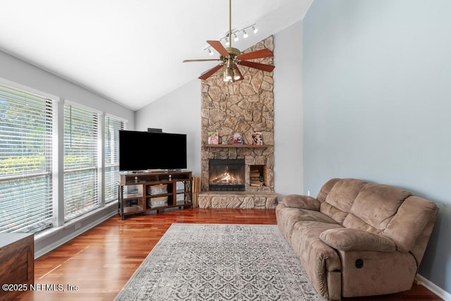 living room featuring hardwood / wood-style floors, a stone fireplace, rail lighting, vaulted ceiling, and ceiling fan