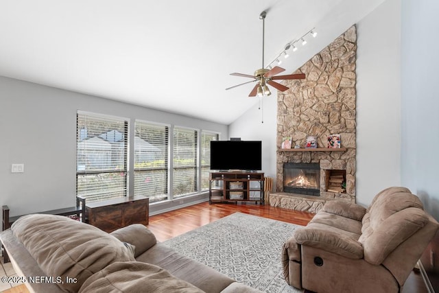 living room with ceiling fan, light wood-type flooring, a stone fireplace, and vaulted ceiling