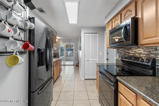 kitchen featuring light tile patterned floors, stainless steel fridge, tasteful backsplash, dark stone countertops, and black range with electric stovetop